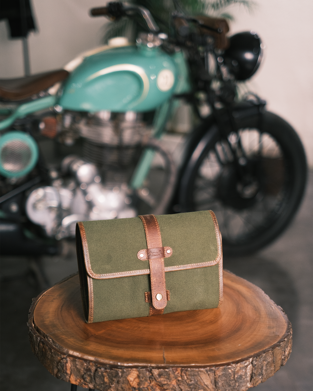 Green leather care kit bag on a wooden surface with a motorcycle in the background